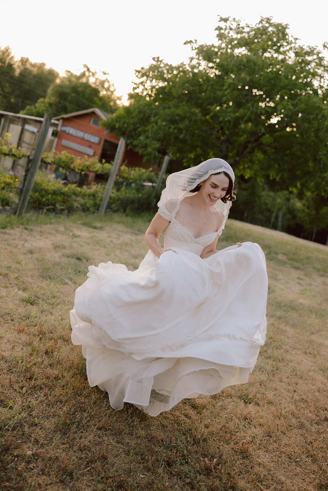 Bride laughing as she twirls her gown at golden hour in the vineyard